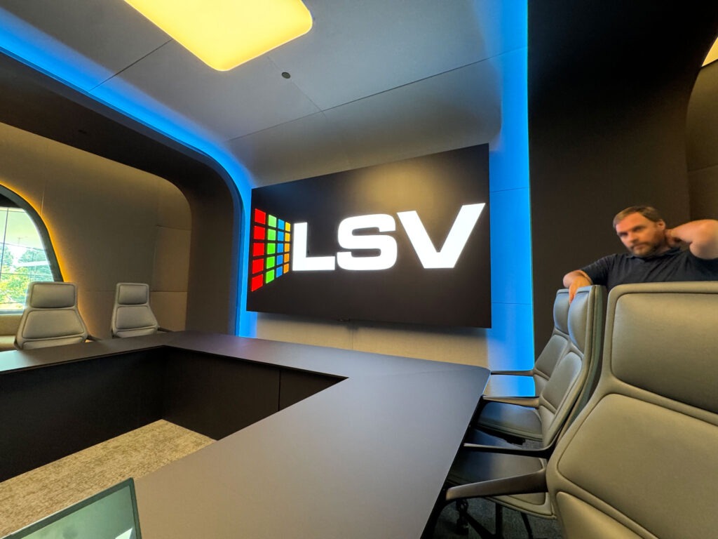 Modern conference room featuring a large screen displaying "LSV," sleek gray chairs, and blue ambient lighting. Ideal for business meetings.