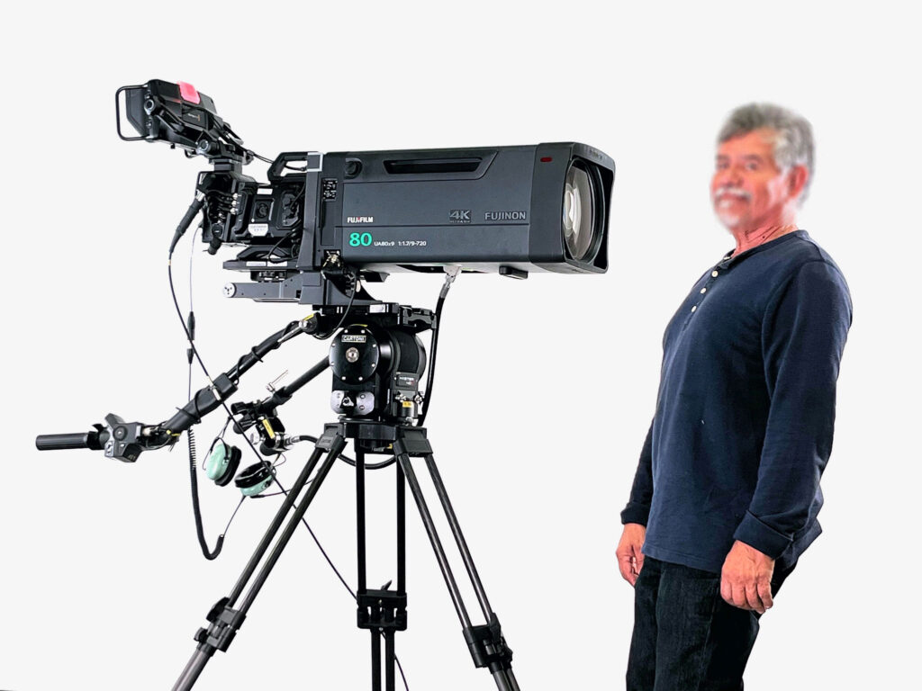 A man stands beside a professional 4K camera on a tripod, showcasing video production equipment critical for filming and broadcasting.