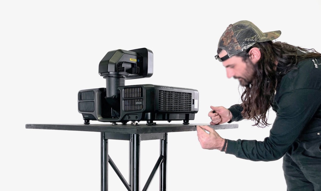 A man adjusts a black Epson projector on a table, preparing it for use in a likely presentation or event setting.